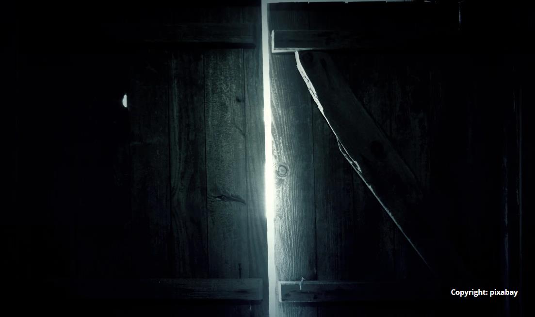 dunkles Scheunentor von innen, durch einen Türspalt fällt Licht